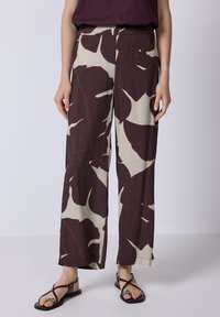Wijdvallende broek met een bladerenpatroon in bordeauxrood en roomwit, met een elastische tailleband en lichte stof. Draagt gecombineerd met platte sandalen.