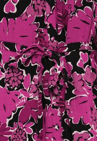 Cvečni obleki, ki ima velike roza in bele rože na črnem ozadju, z vezanjem v pasu in nabranim teksturo.