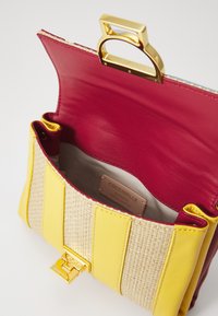 Gul og beige stribet taske med en gyldent spænde, der har en rød læderindvendig og et label, der står "Coccinelle Authentic Italian Leather."