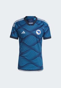 Niebieska piłkarska koszulka w wzór fal z dekoltem w serek, trzema białymi paskami na ramionach oraz okrągłą naszywką z mapą i kolorami Bośni.
