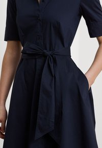 Navy blue shirt dress in cotton blend featuring short sleeves, a button front, and a tied waist belt with side pockets. Smooth texture.