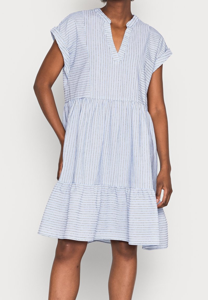 Femme portant une robe ample à manches courtes, longueur genoux, avec des fines rayures bleues verticales et horizontales et un col en V.