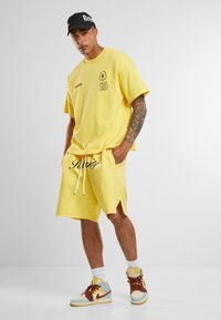 Yellow cotton oversized t-shirt with logo and number graphics, paired with matching shorts. Complemented by multi-color sneakers and white socks.