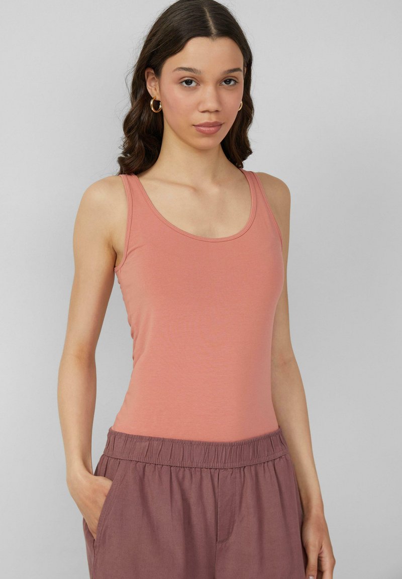 Perzikkleurige tanktop met ribbelstructuur, voorzien van een ronde hals en smalle bandjes. Het model draagt deze met bijpassende losse broek.