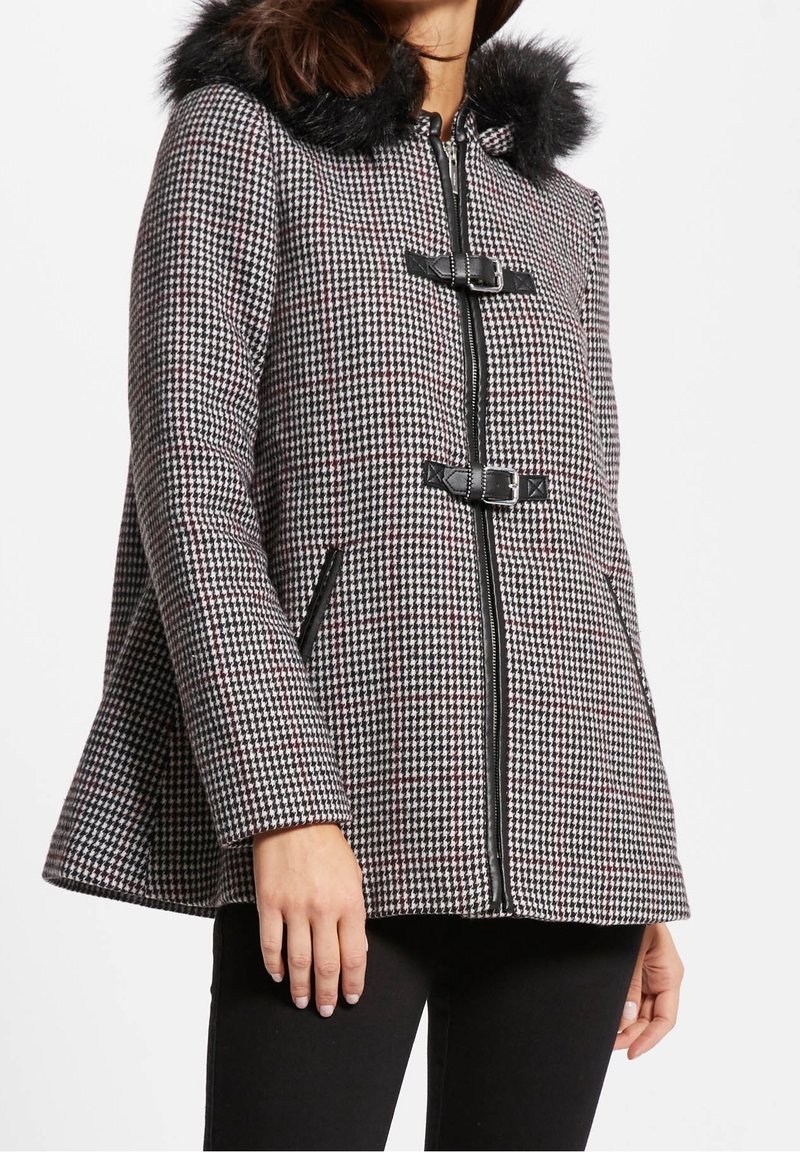 Cappotto houndstooth in bianco e nero con cappuccio foderato in pelliccia, chiusura a zip e fibbie nere. Presenta tasche laterali e un design con orlo svasato.