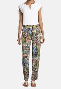 Witte korte mouwen top met een V-hals, gecombineerd met beige broek met een kleurrijk bloemen- en luipaardpatroon, en lichte sandalen.