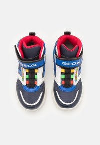 Blue and white sneakers with a textured fabric, Velcro strap, and colorful accents. Features a red lining and a logo. Rounded toe design.