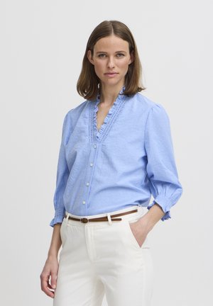 Light blue shirt with ruffled neckline, button-down front, and gathered sleeves. Paired with white pants and a brown belt.