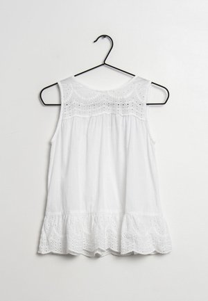 Weiße ärmellose Baumwollbluse mit Lochstickerei am Ausschnitt und gerafftem Saum, an einem schwarzen Kleiderbügel vor einfarbigem Hintergrund hängend.