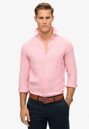 Camicia a righe rosa con colletto rialzato, maniche lunghe arrotolate ai polsi, abbinata a una cintura marrone e pantaloni scuri.