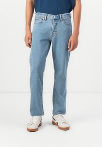 Lichtblauwe denim jeans met een rechte snit, subtiele textuur, vijf zakken en gestikte accenten. Draagt met witte sneakers met bruine zolen.