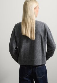 Suéter de punto gris con hombros caídos, diseño corto, tejido texturizado y dobladillo acanalado, combinado con jeans de denim azul oscuro.