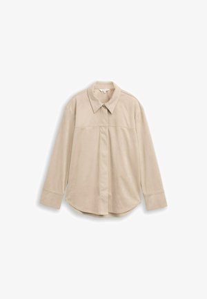 Beige hosszú ujjú ing, hegyes gallérral, elülső panel varrással és ívelt aljjal. Simább, könnyű anyagból készült.