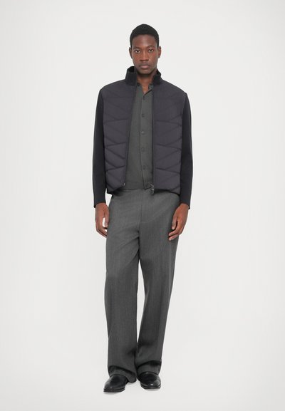 Quilted black jacket with high collar, paired with a dark gray button-up shirt and light gray wide-leg pants. Slim shoes complete the look.