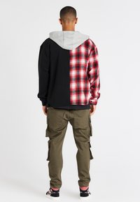 Svart och röd rutigt oversized hoodie med grå huva, med kontrasterande sidor. Bärs med olivfärgade cargobyxor och sportiga svarta skor.