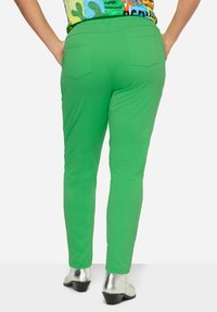 Groene, stretch broek met een strakke pasvorm, met achterzakken en een elastische tailleband, gecombineerd met zilveren schoenen.