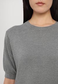 Grå strikket kortermet topp med rund hals og lett puffede ermer, med en glatt, fin tekstur.