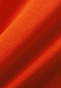 Tissu orange vif avec une texture fine en tricot et des plis doux créant des ombres et des reflets délicats.