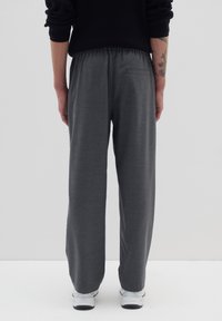 Graue Sweatpants mit einem entspannten Schnitt, elastischem Bund und einer Gesäßtasche. Kombiniert mit weißen Sneakers. Weicher, strukturierter Stoff.