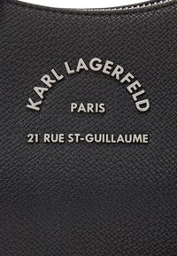 Black textured leather bag featuring embossed silver brand logo "KARL LAGERFELD PARIS" with "21 RUE ST-GUILLAUME" beneath.