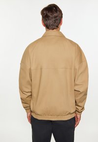 Khaki Bomberjacke mit lockerem Schnitt, elastischen Bündchen und einem schlichten Design. Glatte Textur und kontrastierende Nähte.