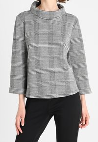 Top de cuadros en gris y negro con cuello de embudo, mangas largas y textura suave; combinado con pantalones negros. Silueta simple y estructurada.