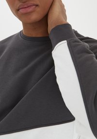 Gray and white long-sleeve sweatshirt with a crew neck, featuring color-block design, smooth texture, and contrasting sleeves.