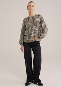 Blus med leopardmönster och långa, puffiga ärmar samt rundad halsringning, tillsammans med svarta vida jeans och svarta slip-on skor.