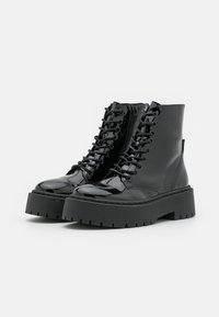 Bottines en cuir verni noir avec une semelle épaisse noire, dotées de lacets, d'une fermeture éclair sur le côté et d'un capuchon de orteil texturé.