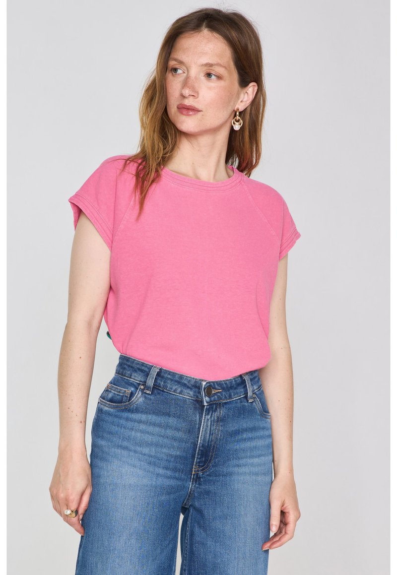 T-shirt in cotone rosa con maniche corte, scollo rotondo e vestibilità rilassata, abbinato a jeans in denim blu a vita alta.