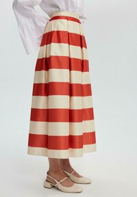 Pleated long skirt in cream and red horizontal stripes, made of smooth fabric. Paired with beige patent slingback shoes.