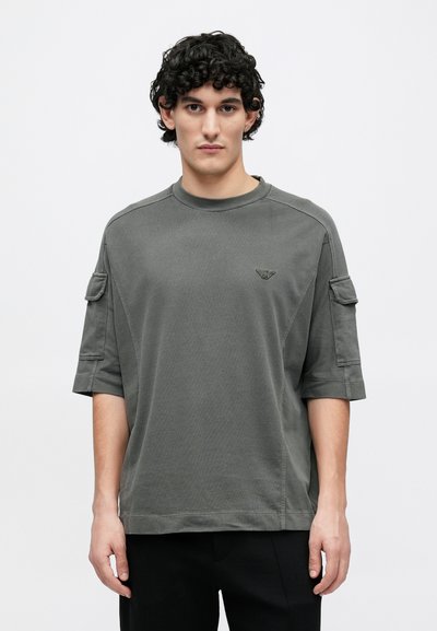 Šedé bavlněné tričko s krátkými rukávy, kulatým výstřihem a bočními kapsami. Na hrudi je vyšitá logo a má volný střih.