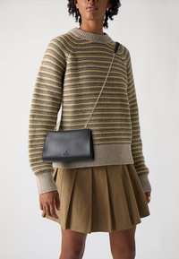 Must mustrisest nahkrist crossbody kott, millel on minimalistlik disain, sujuv tekstuur ja diskreetne bränding. Kandmise koos triibulise sviitriga ja volditud seelikuga.