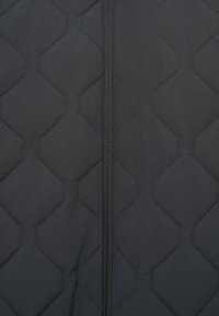 Czarna pikowana kurtka z sześciokątnym wzorem, z centralnym zamkiem błyskawicznym. Materiał wydaje się gładki z delikatnym połyskiem.