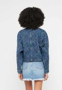 Krótka kurtka dżinsowa z wzorem diamentu, długimi rękawami i surowym wykończeniem. Nosi się ją na jasnoniebieską mini spódnicę dżinsową.