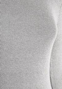 Gros plan sur un tissu côtelé rayé verticalement blanc et noir épousant une surface courbe, probablement une partie d'un vêtement ajusté.