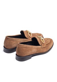 Mocassini in suede marrone con un accento in metallo dorato, suola nera in gomma piatta e fodera interna liscia; design minimalista.