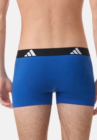 Boxers en coton stretch bleu avec une ceinture élastique noire présentant un design à trois rayures blanches dans le dos.