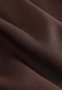 Dark brown woven fabric with soft folds and a smooth texture, highlighted by subtle lighting across the surface.