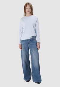 Hellblaues Langarmshirt mit Rundhalsausschnitt, kombiniert mit weitem blauen Jeanshose. Glatter Stoff mit lässiger Passform, ohne sichtbare Muster oder Akzente.