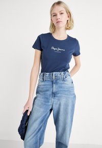 Navy katoenen t-shirt met witte "Pepe Jeans London" logo, gecombineerd met lichtblauwe hoge taille denim jeans, textuurstof en een losse pasvorm.