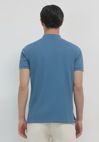 Polo shirt blu a maniche corte con finitura testurizzata, colletto e fessure laterali. Realizzato in un materiale leggero, progettato per una vestibilità aderente.