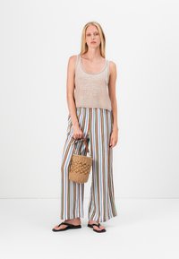 Helles beige Tanktop, gestreifte weit geschnittene Hose in verschiedenen Farben und eine geflochtene Handtasche. Das Model trägt schwarze Flip-Flops. Schlichtes, lässiges Outfit.