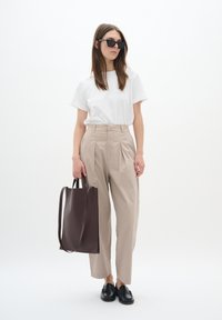 Beige high-waisted trousers, white short-sleeve shirt, black loafers, and a dark brown tote bag. Model wearing black rectangular sunglasses.