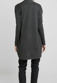 Langärmlige, dunkelgraue Strickjacke aus weichem Strickstoff, mit rundem Halsausschnitt und geradem Saum, getragen über schwarzen Hosen.