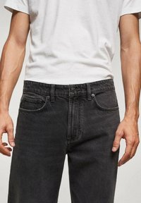 Jean denim noir avec une coupe droite classique, doté de poches avant et d'une fermeture éclair. Le tissu présente une texture subtile et un aspect délavé.