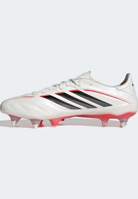 Λευκό ποδοσφαιρικό παπούτσι με μαύρες ρίγες, ασημί λεπτομέρειες και υφή στην επιφάνεια. Διαθέτει ροζ και διάφανο εξωτερικό πέλμα με καρφιά για καλύτερη πρόσφυση.