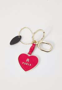 Crvena kožna privjesak u obliku srca s zlatnim dijelovima i utisnutim logotipom "FURLA". Sadrži zlatni lanac i crnu oznaku.