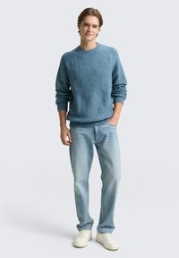 Jasnoniebieski prążkowany sweter z okrągłym dekoltem, noszony z jasnymi dżinsami i białymi tenisówkami. Sweter ma długie rękawy i luźny krój.