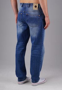 Blue denim jeans with a faded finish, six pockets, copper rivets, and a branded leather patch at the waistband. Straight-leg design.